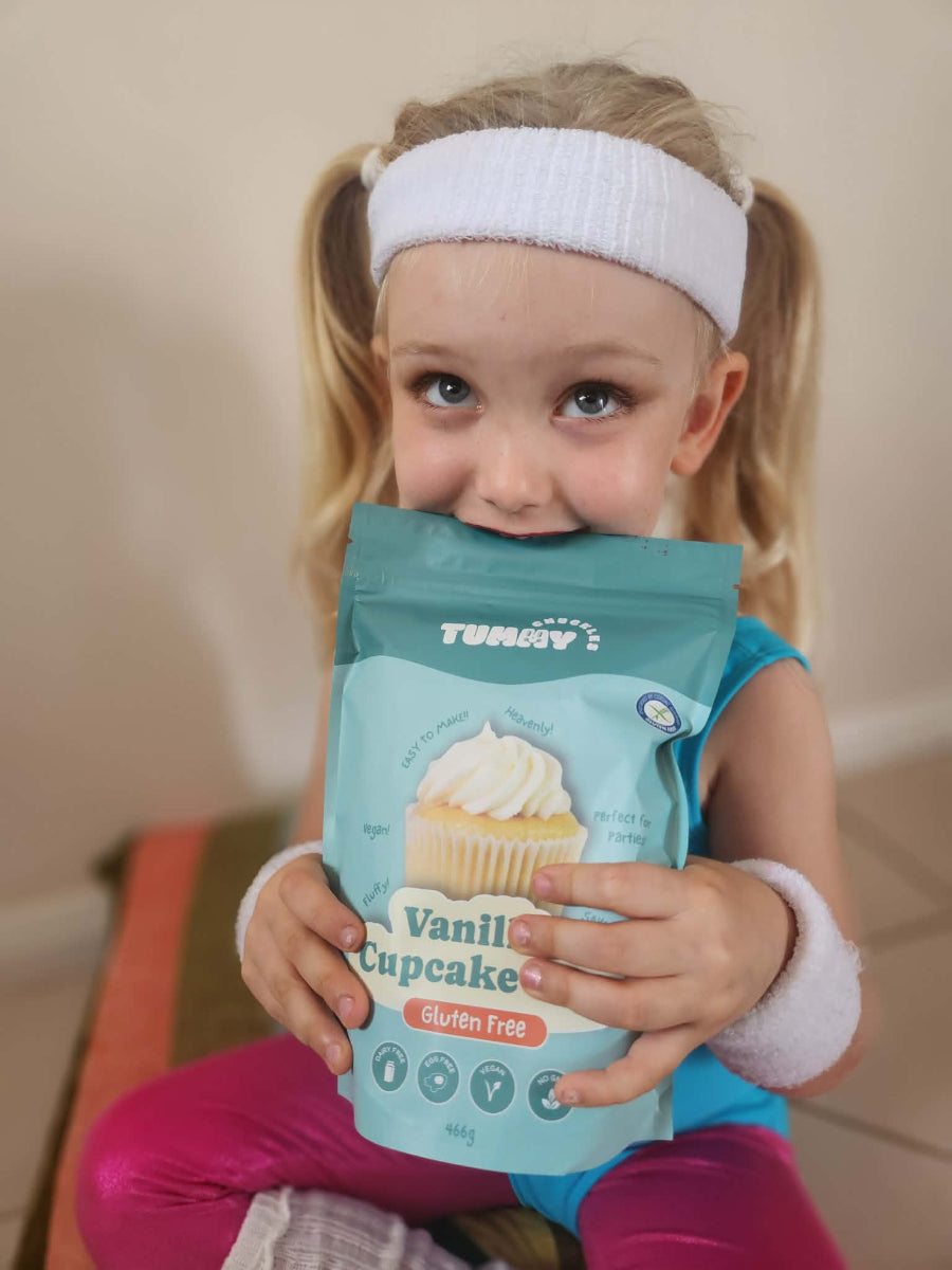 Child holding a Tummy Chuckles Vanilla Cupcake package with a plain background