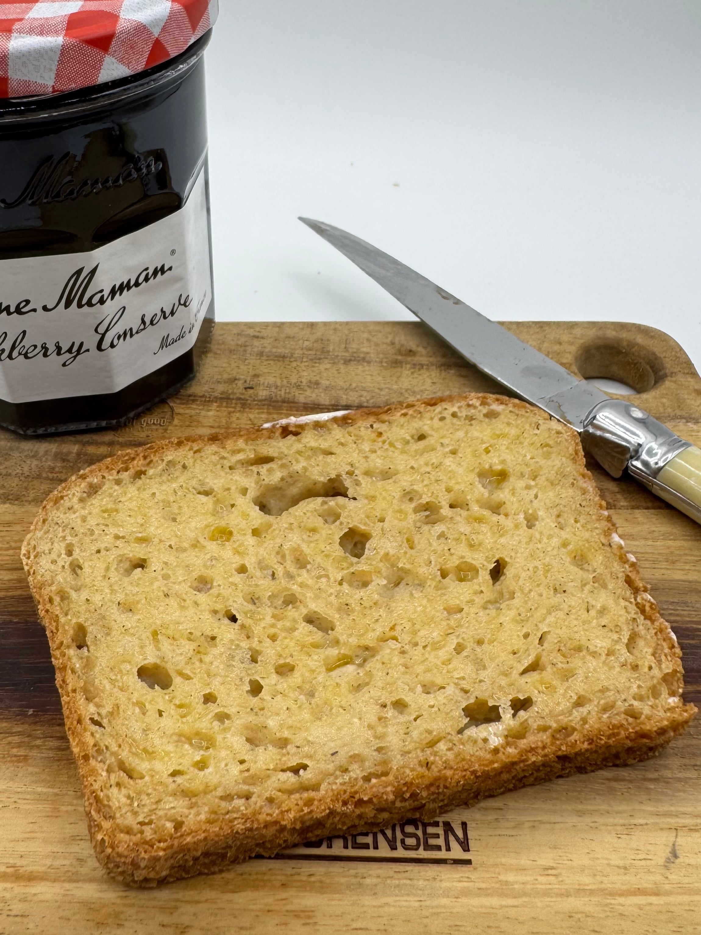 Slice of bread toasted on a cutting board with a jar of preserve and knife in the background