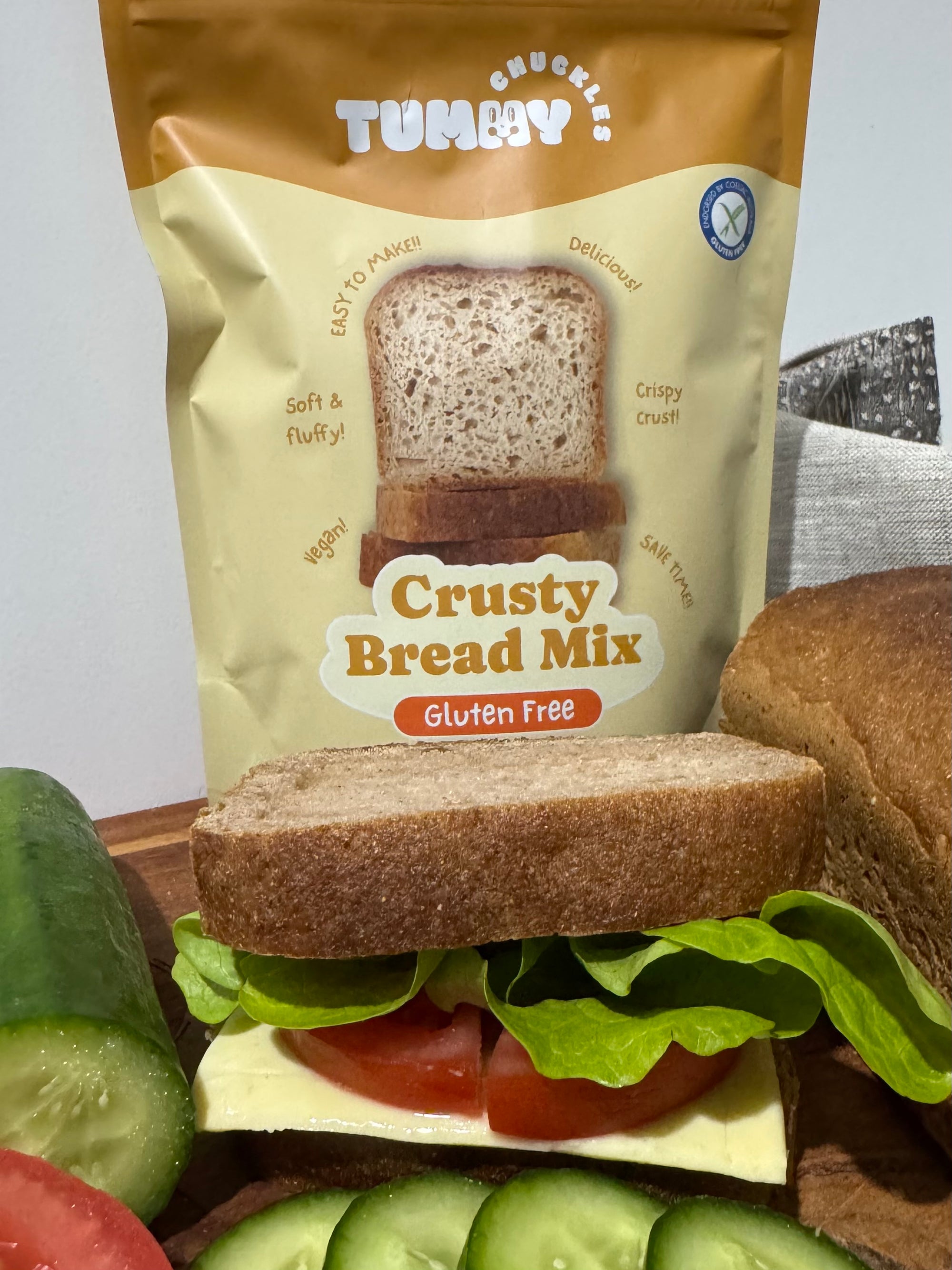 Tummy Chuckles Crusty Bread Mix package with a sandwich and vegetables on a gray background